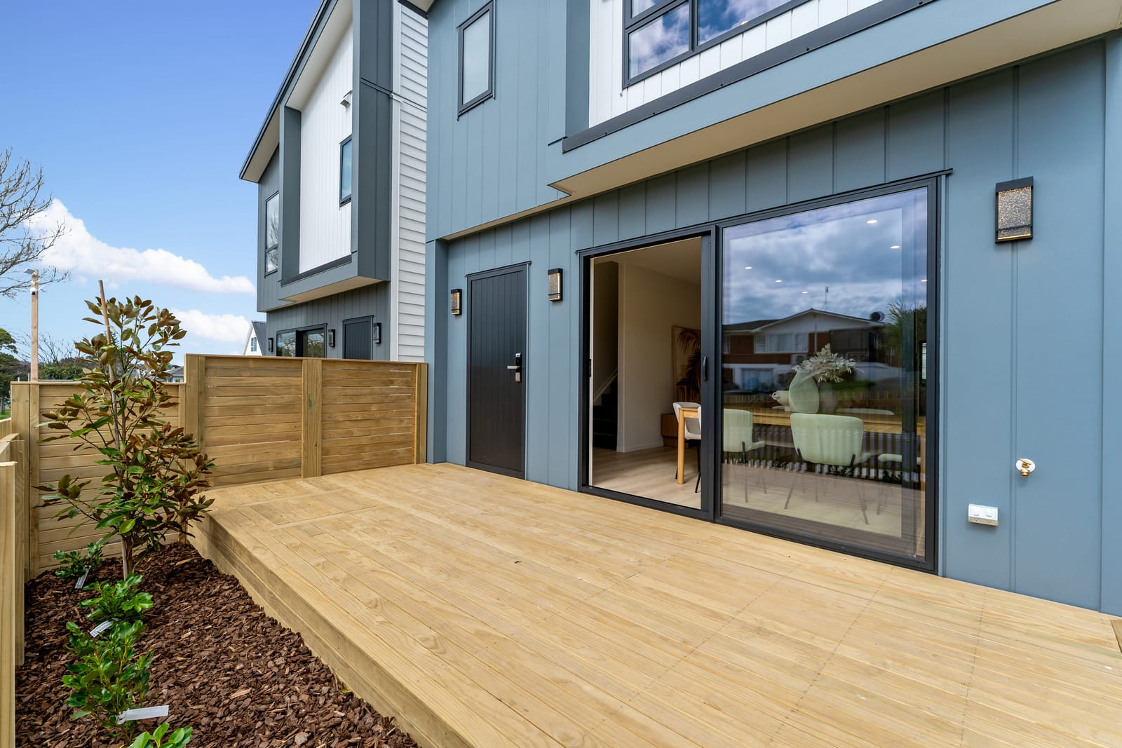 A new timber deck outside the living room, with sliding doors and a fenced, planted garden