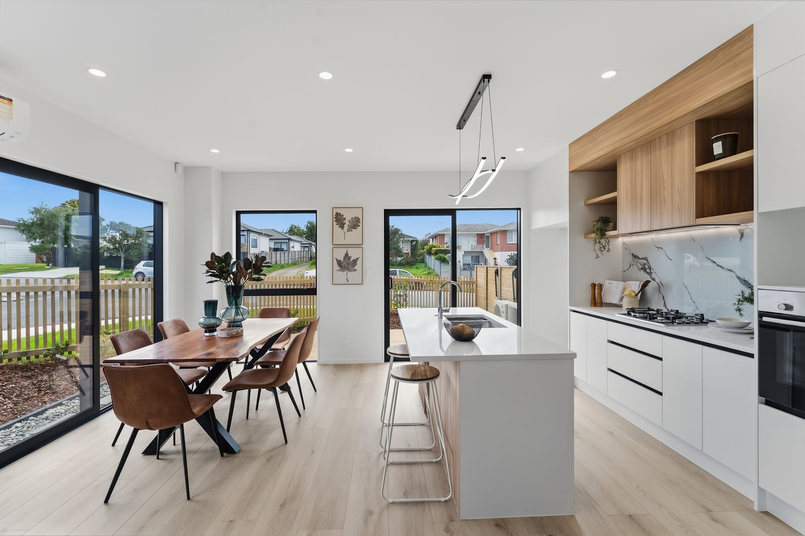 Dining area and kitchen with light timber-look floors, a timber table, black-framed sliding doors and an island bench