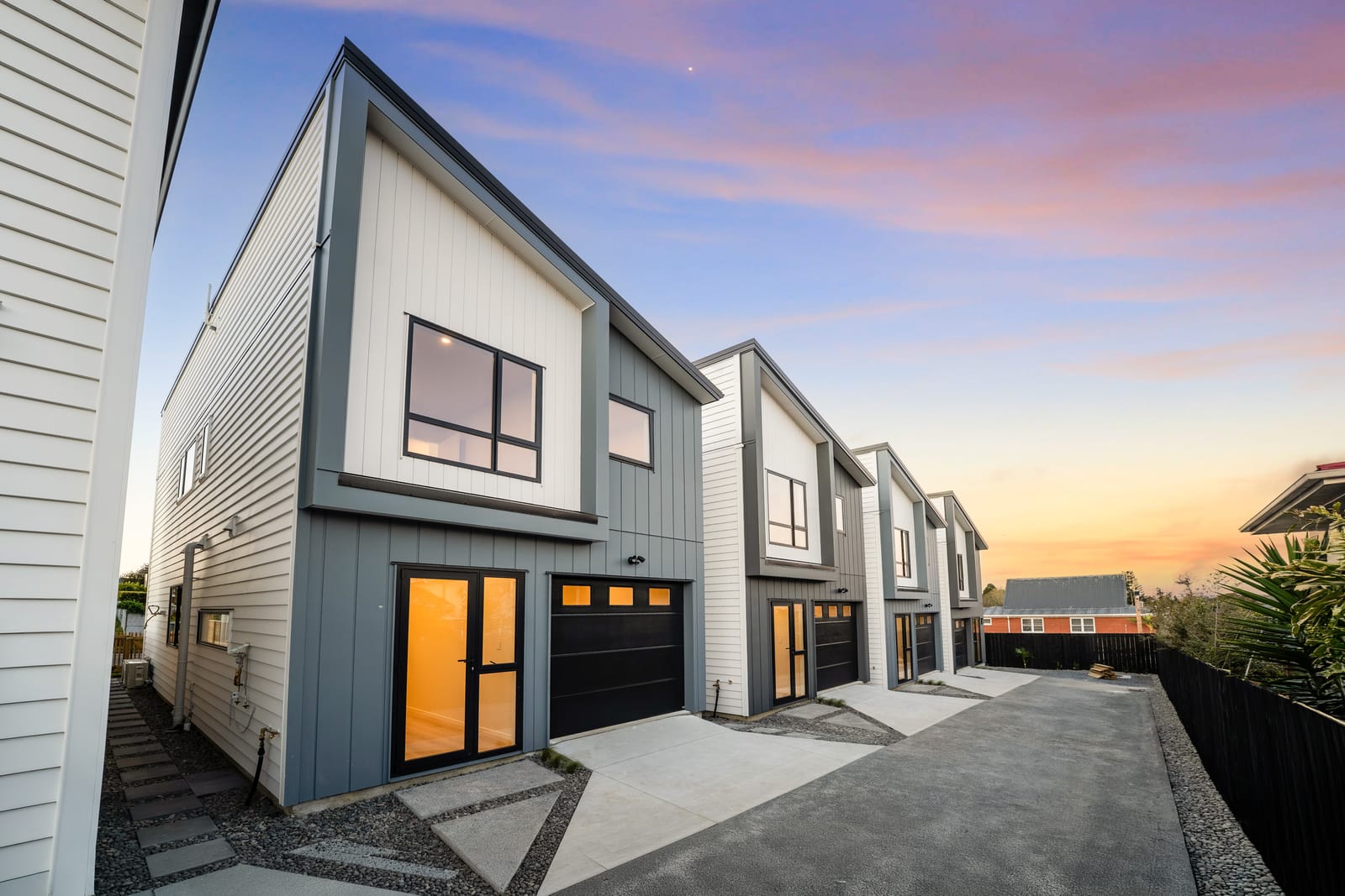 The driveway at dusk between white and dark grey cladding, garage doors along one side