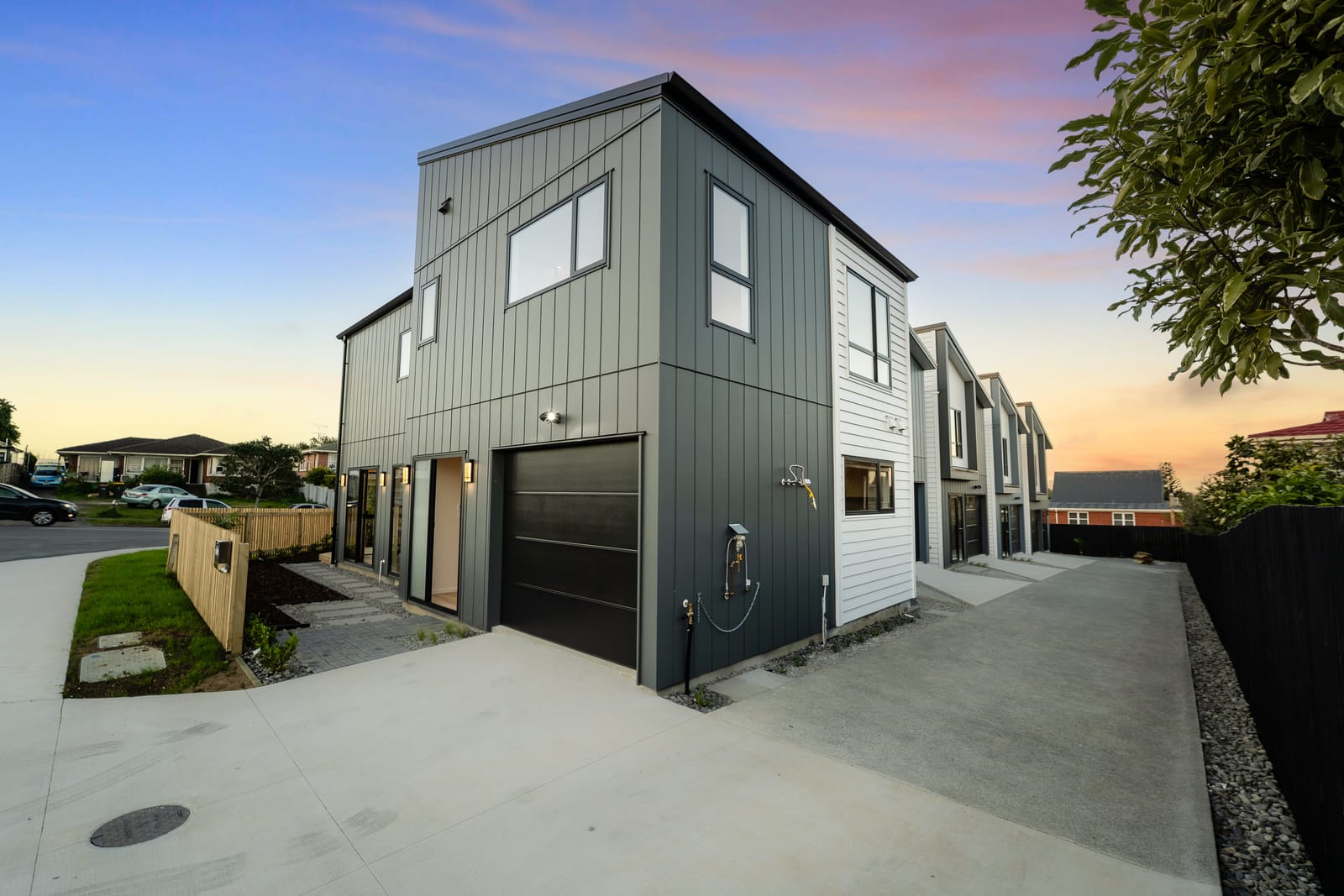 The front home at the entrance to the shared driveway at dusk, its garage facing the drive and the other homes beyond