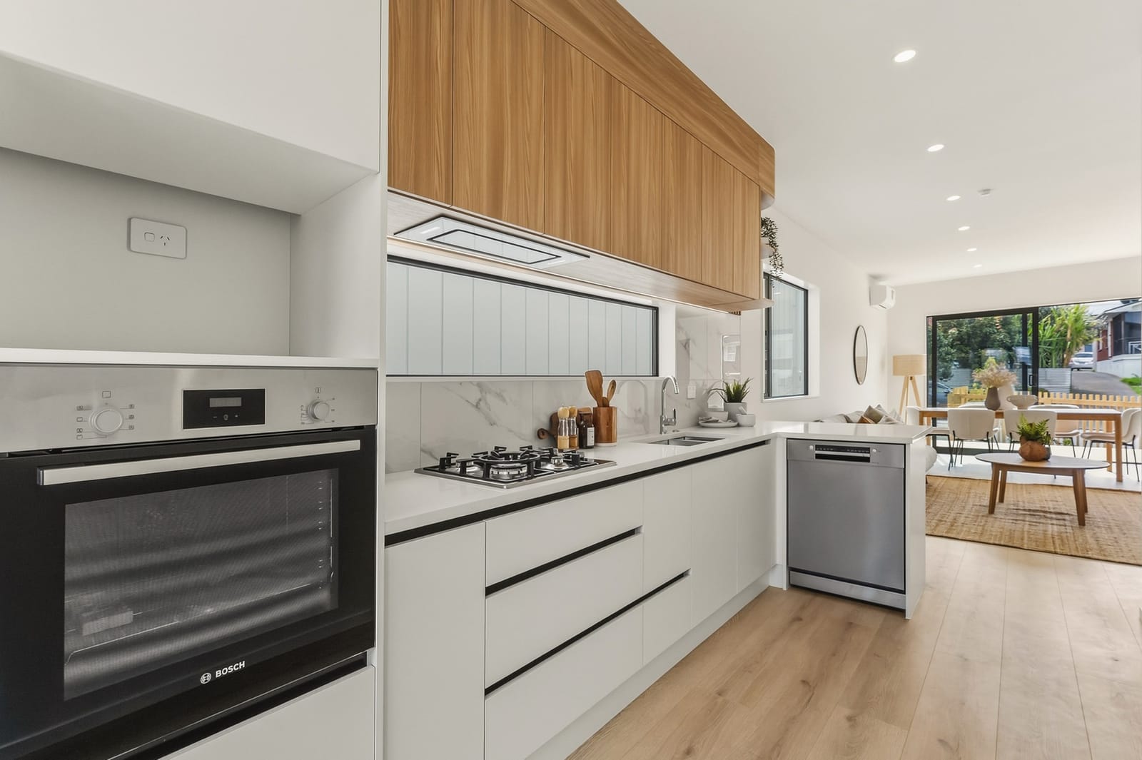 Kitchen with a Bosch wall oven, gas hob and dishwasher, looking through to the living area