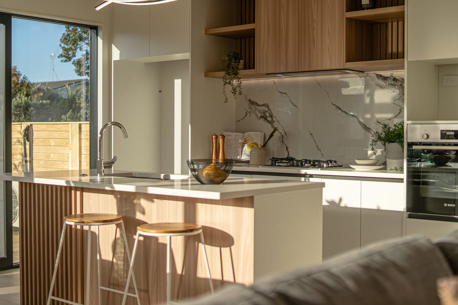 Kitchen with a gas hob, marble-look splashback, open timber shelving and island seating