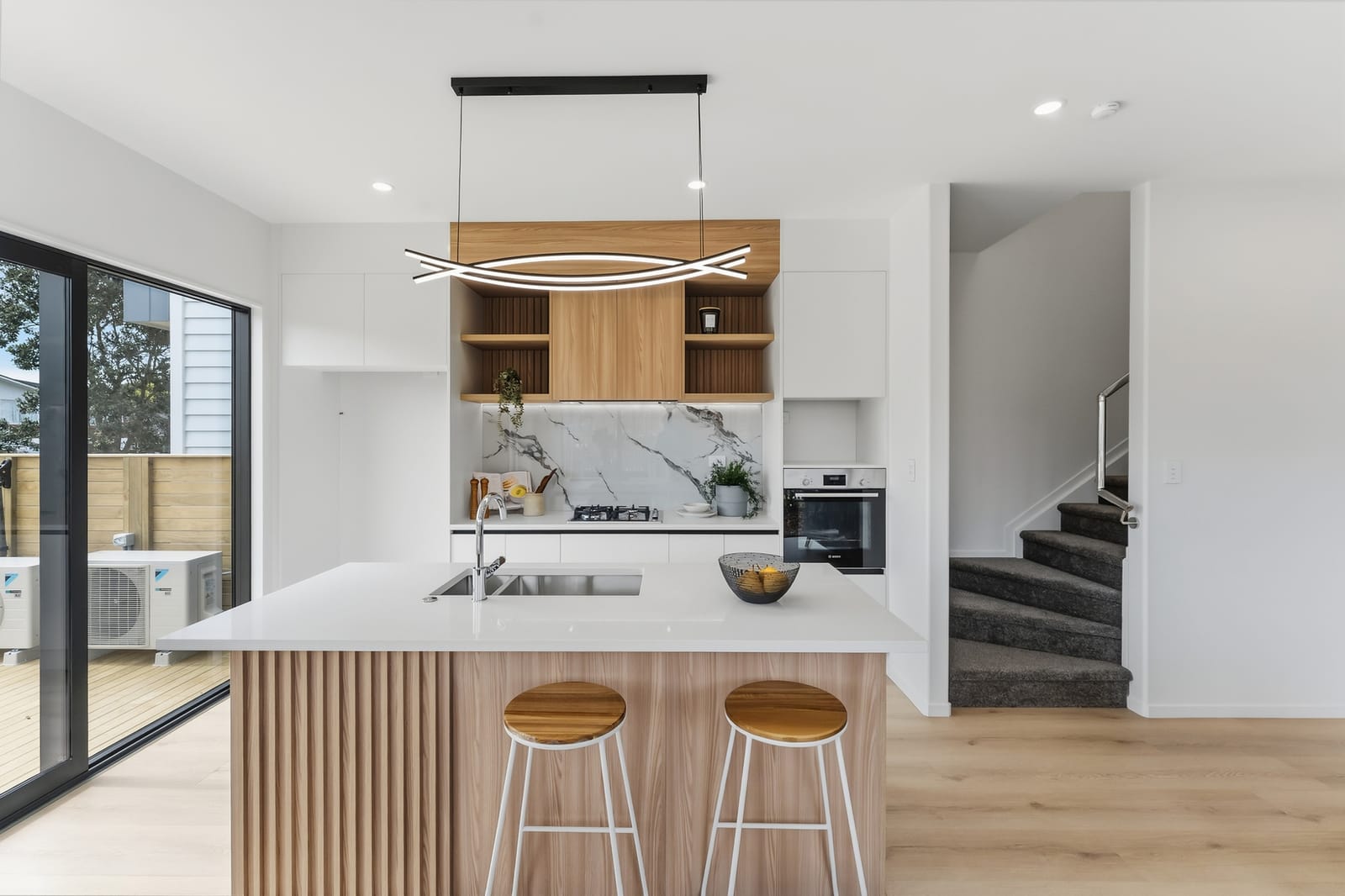 Kitchen with a fluted timber island, white benchtop, marble-look splashback and a sculptural pendant light
