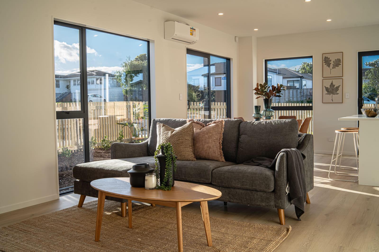 Living room in afternoon light with a grey sofa, oval coffee table and large black-framed windows