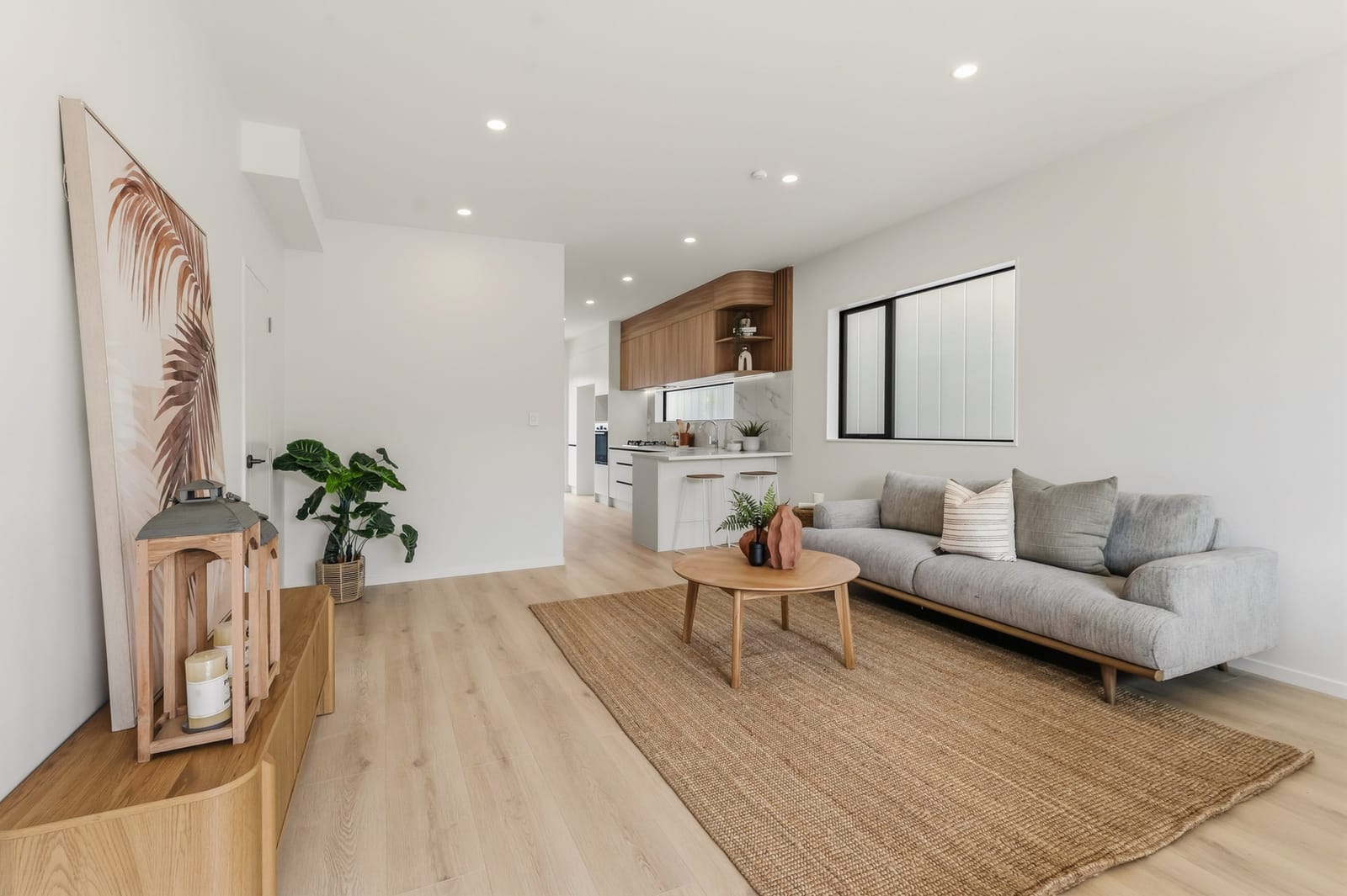 Bright lounge with a jute rug and round coffee table, the kitchen behind