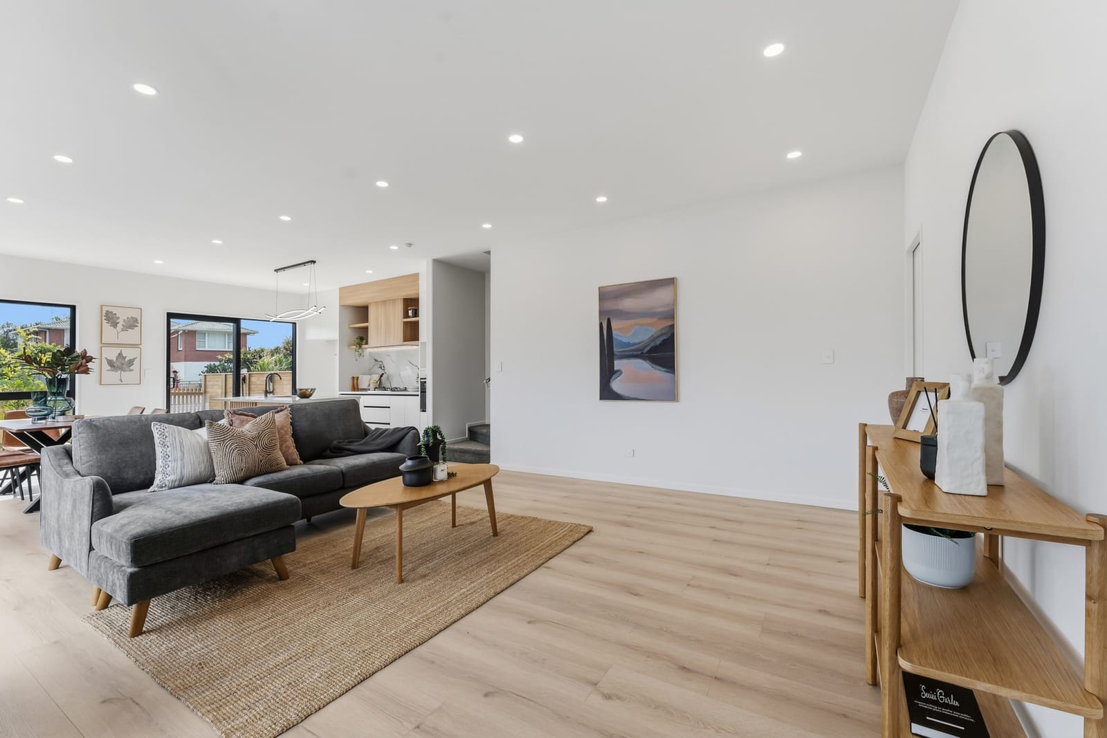 Open-plan living with a chaise sofa, round mirror and timber console