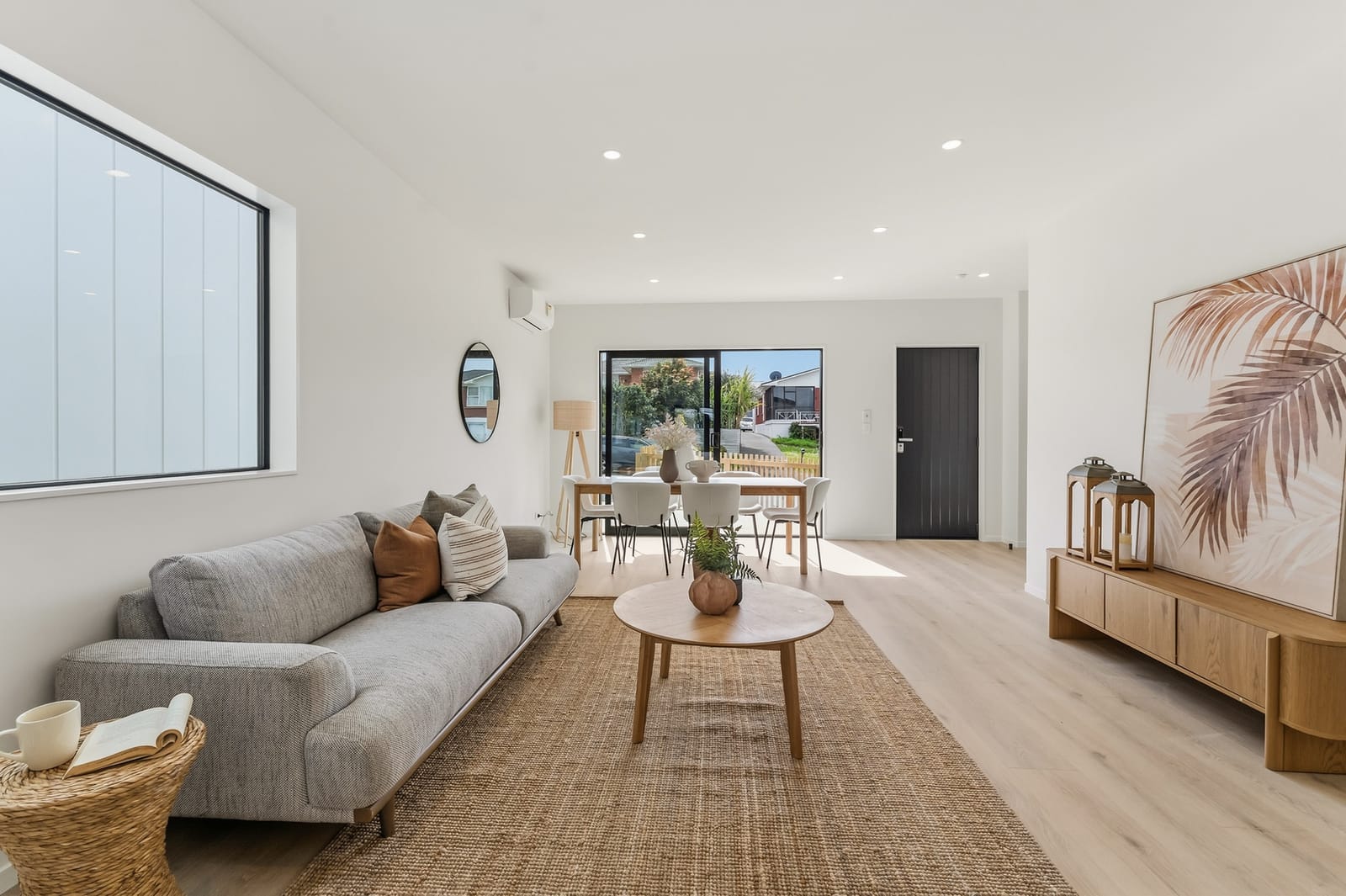 Open-plan living room with a light grey sofa, jute rug and timber console, the dining area and front door beyond