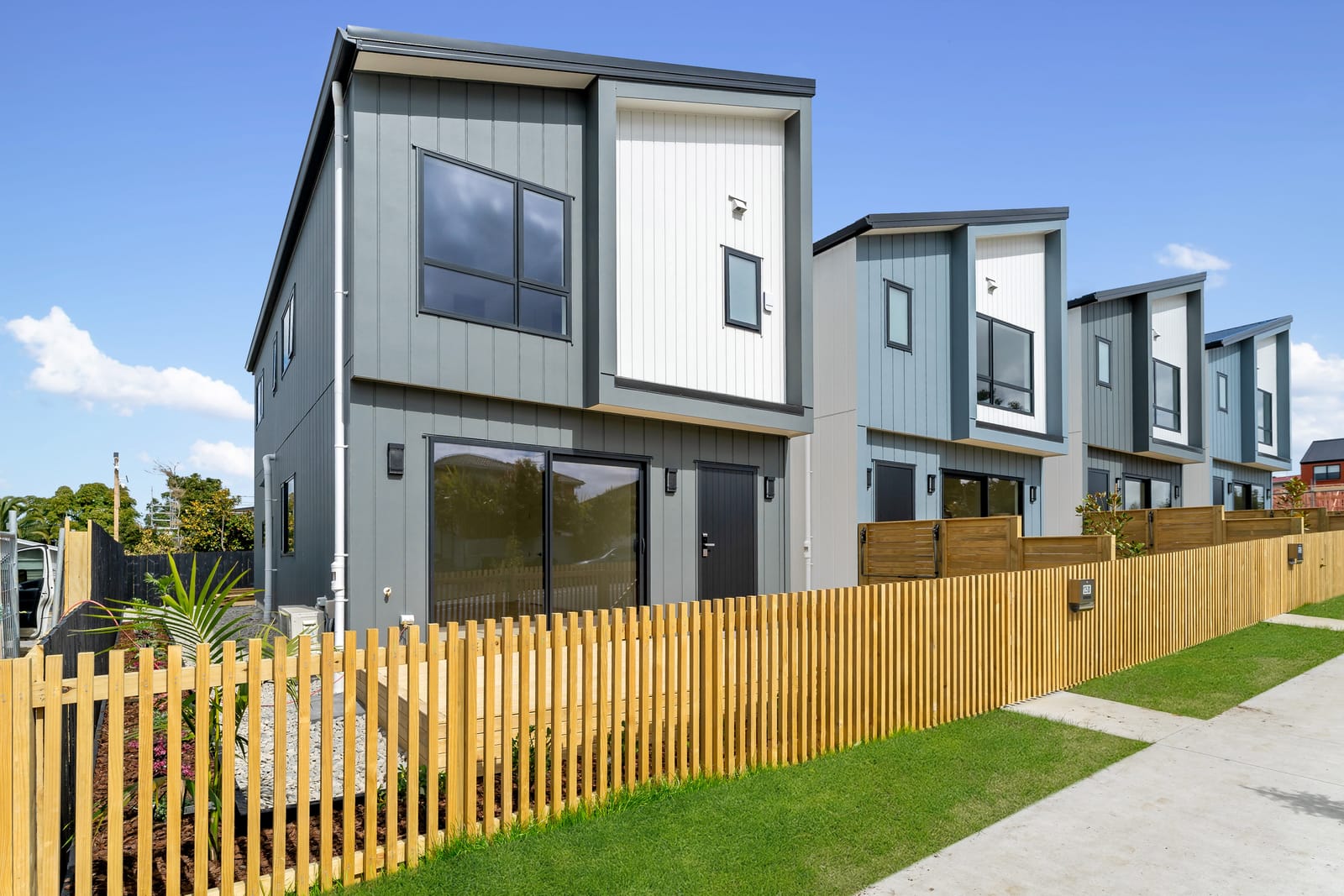 Looking along the row of homes in daylight, blue-grey and white cladding above the timber fence