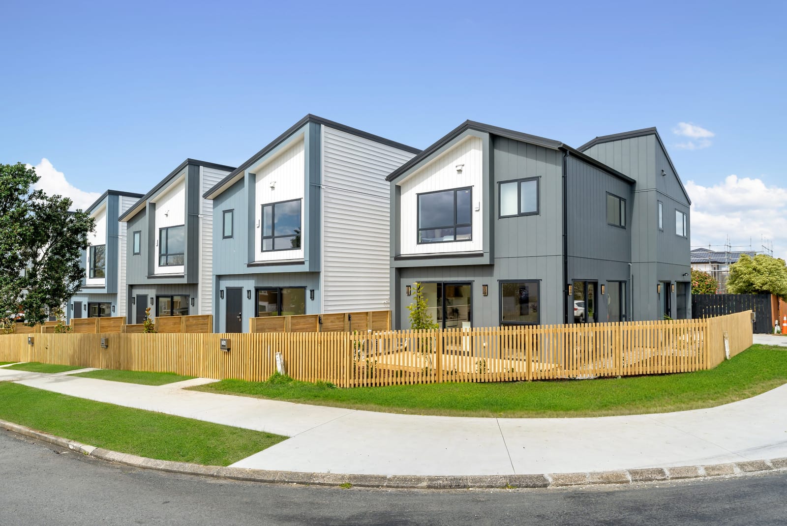 The row of new homes by day behind a new slatted timber fence, with lawn and footpath in front