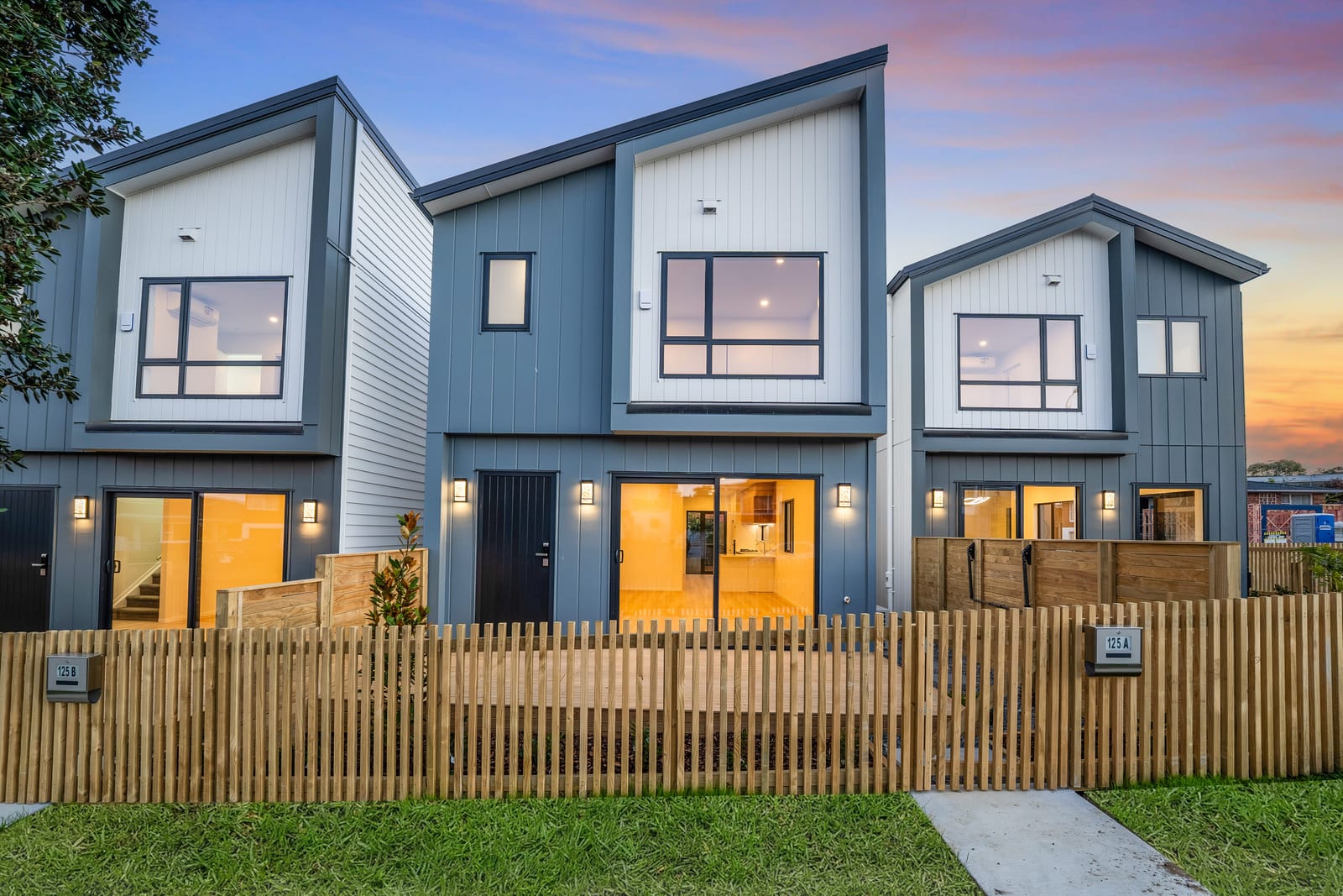 Three of the homes seen from the street at dusk, each behind its own fenced front garden