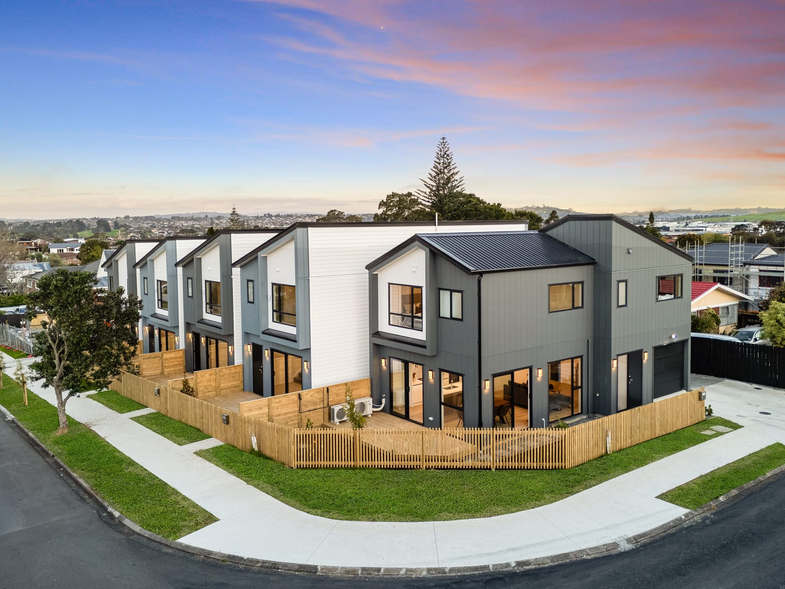 Elevated twilight view of the five new homes in a row on their corner site, with slatted timber fences and a pink and blue evening sky